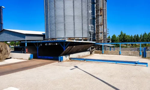 Silos metálicos industriales con estructura azul de carga y descarga en el exterior de una planta.