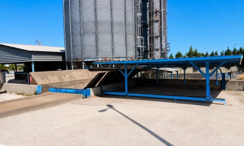 Silos metálicos industriales con estructura azul de carga y descarga en el exterior de una planta.