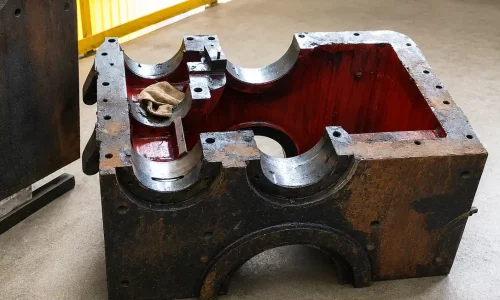 Carcasa metálica industrial desmontada con cavidades mecanizadas en una nave con barandillas amarillas.